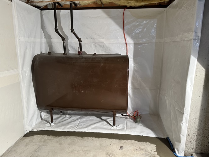 A brown tank positioned in a room surrounded by visible pipes and ductwork on the walls and ceiling.